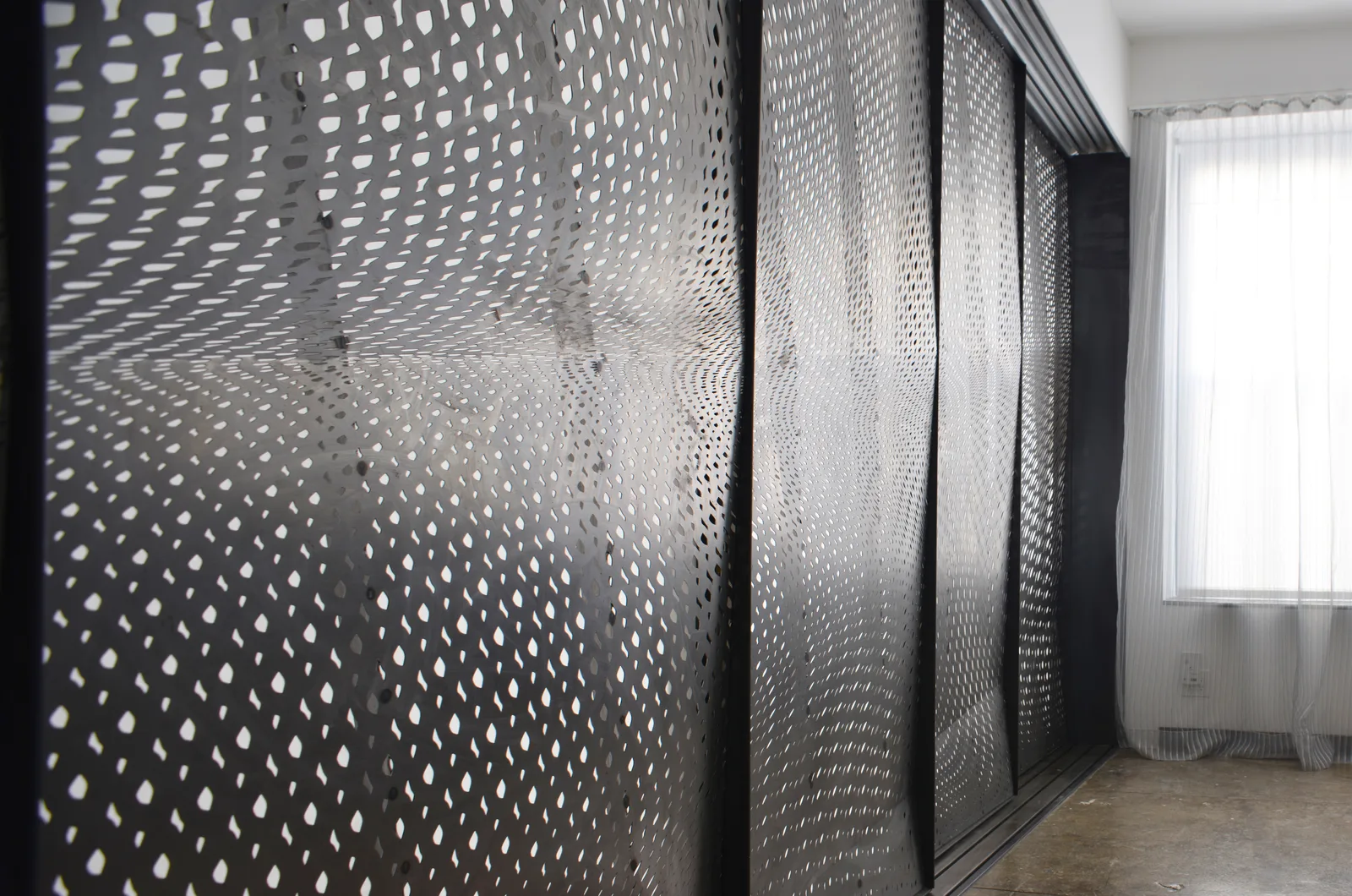 A perforated white screen wall in a dark room, its pattern graded from dense to open across the surface.