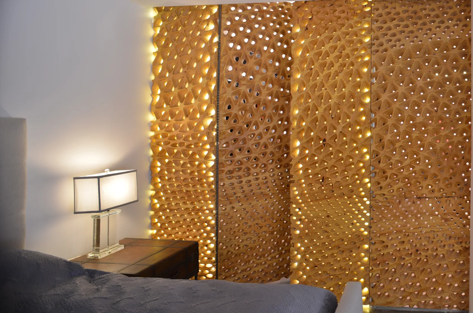 Warm backlit perforated panels forming a partition beside a lamp and low console.
