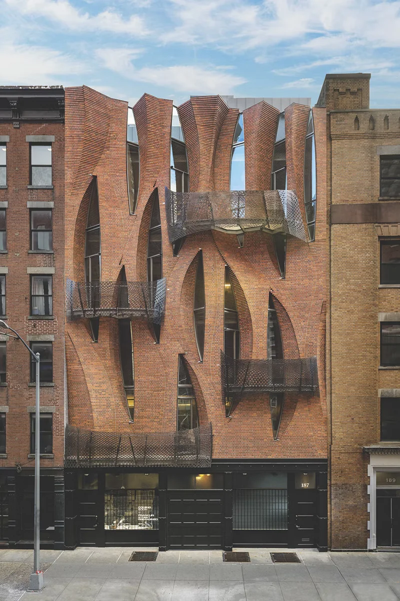 A brick townhouse facade whose surface folds into tall vertical curves between neighboring buildings.