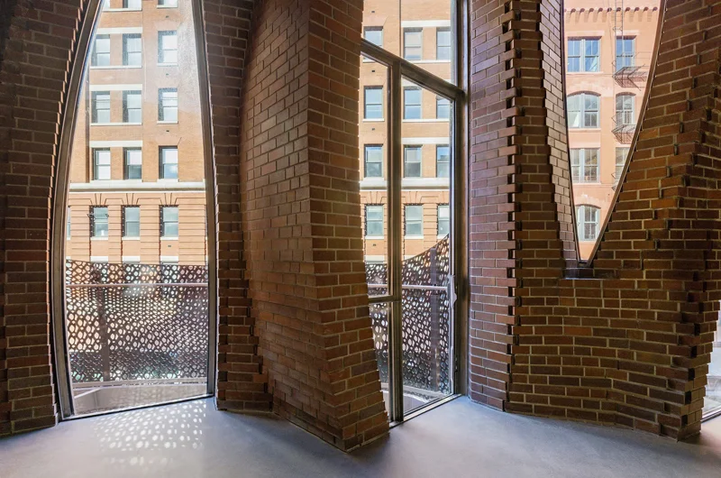Interior view through tall curved brick piers to the street and buildings beyond.